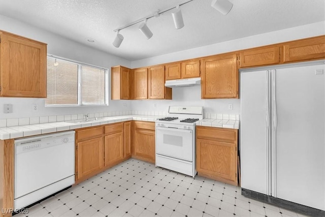 kitchen featuring white appliances, under cabinet range hood, light floors, and a sink