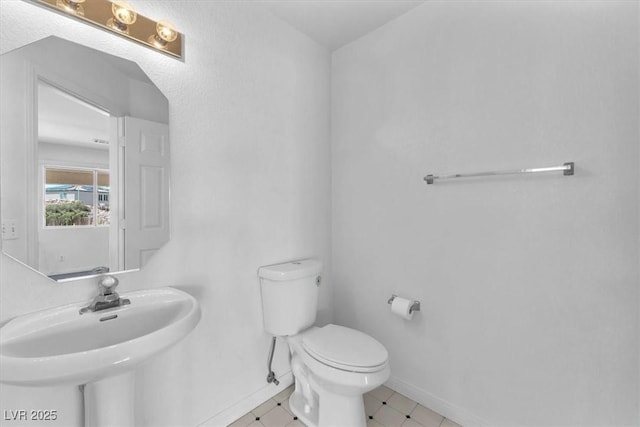 half bathroom with toilet, baseboards, and a sink