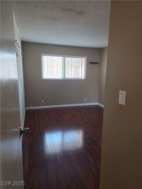 spare room with a textured ceiling, wood finished floors, and baseboards
