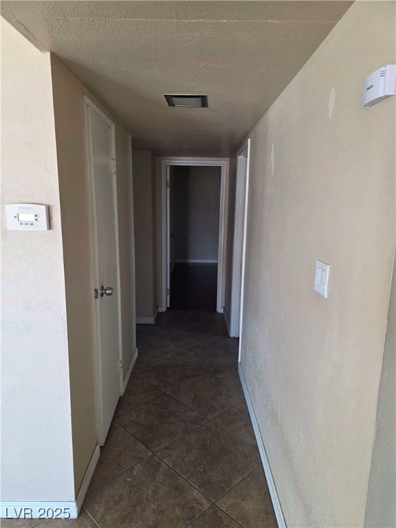 hallway featuring baseboards, dark tile patterned flooring, and a textured ceiling