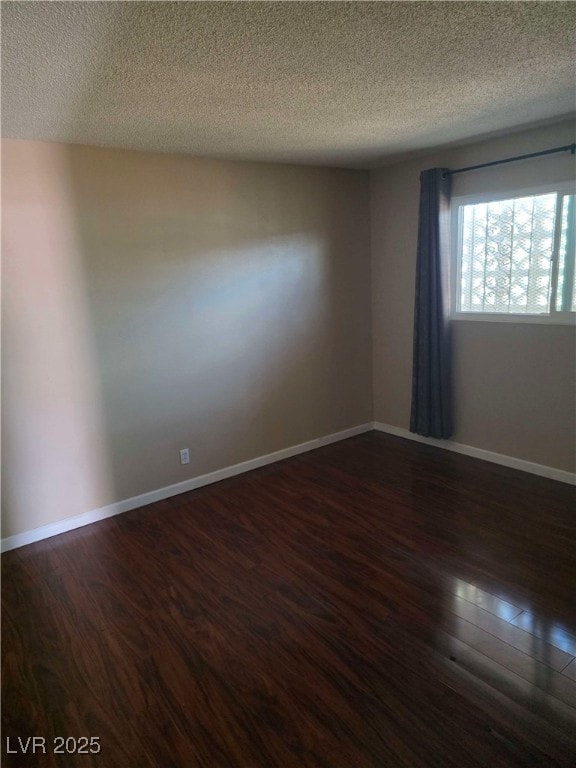 empty room with dark wood-style floors, a textured ceiling, and baseboards