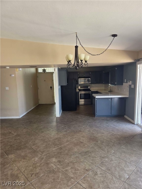 kitchen with stainless steel appliances, light countertops, a chandelier, a peninsula, and dark tile patterned flooring