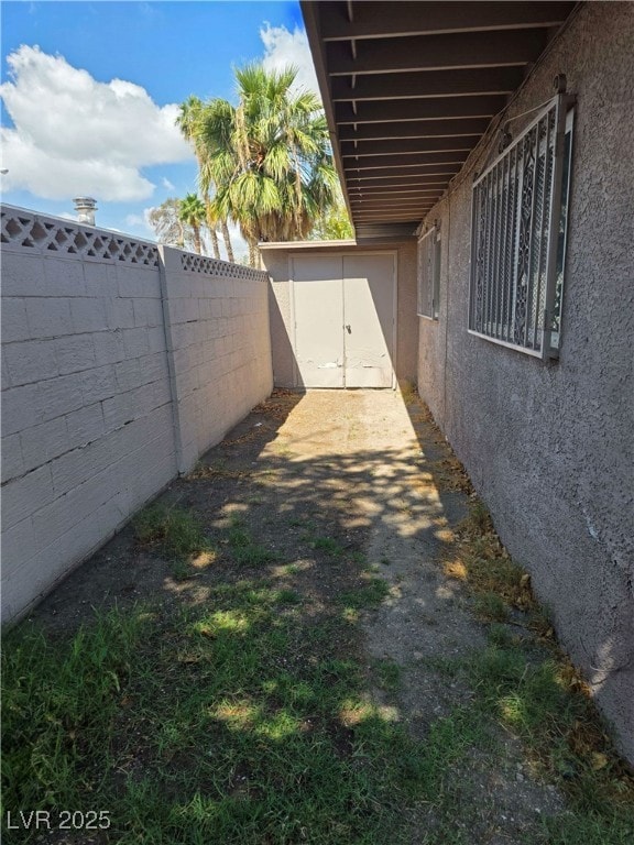 view of side of home featuring stucco siding, a fenced backyard, a shed, and an outdoor structure