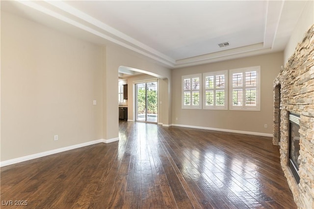 11228 Hedgemont Ave, Las Vegas, NV 89138 - unfurnished living room featuring arched walkways, a tray ceiling, a fireplace, dark wood-type flooring, and baseboards