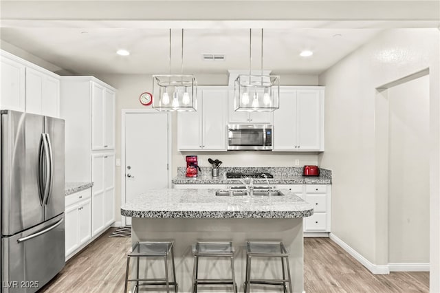 160 Lomita Heights Dr, Las Vegas, NV 89138 - kitchen featuring stainless steel appliances, light wood-style floors, white cabinets, a kitchen island with sink, and light stone countertops