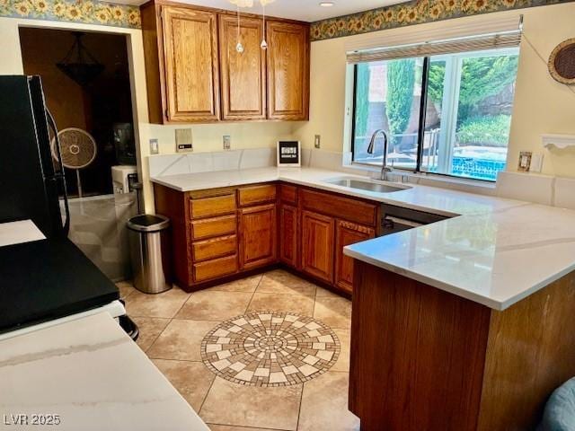 kitchen featuring freestanding refrigerator, a sink, brown cabinets, a peninsula, and light tile patterned floors