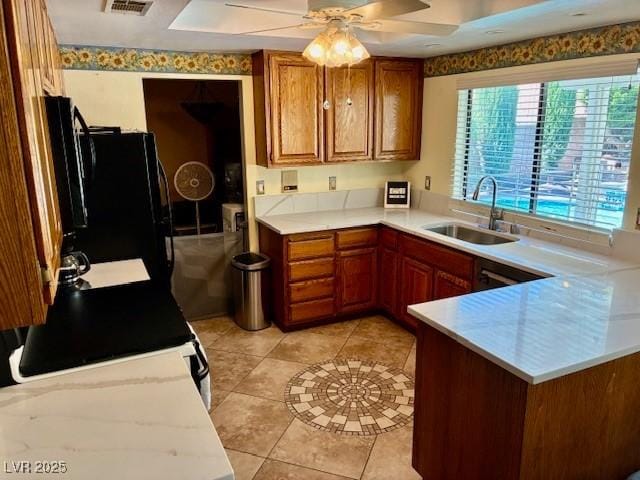 kitchen featuring a sink, brown cabinets, a peninsula, a ceiling fan, and light countertops