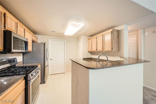 kitchen featuring stainless steel appliances, a peninsula, light brown cabinetry, dark stone countertops, and baseboards