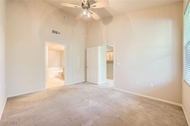 unfurnished bedroom with light colored carpet, high vaulted ceiling, baseboards, and connected bathroom