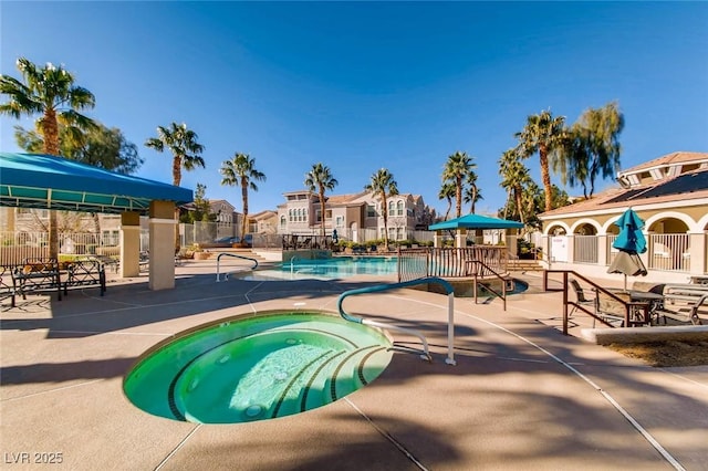 community pool featuring fence, a hot tub, a patio, and a residential view