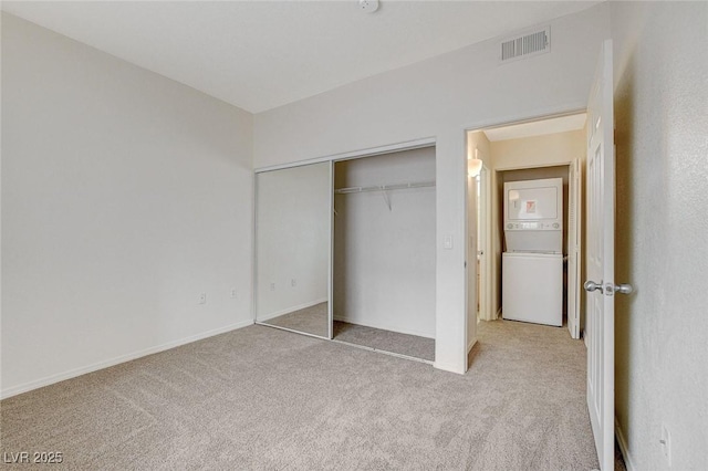 unfurnished bedroom with light carpet, stacked washer / drying machine, a closet, and baseboards