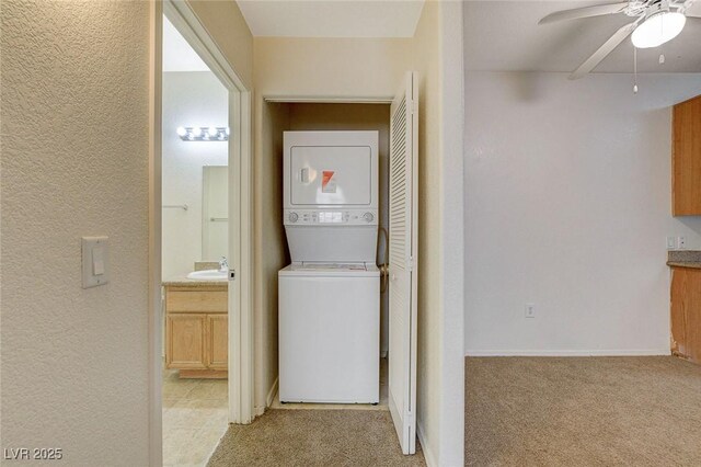laundry room featuring stacked washer / dryer, ceiling fan, a textured wall, and light colored carpet