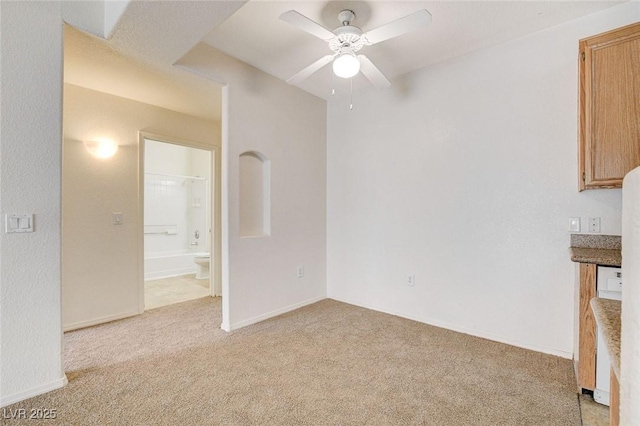spare room featuring light carpet, ceiling fan, and baseboards