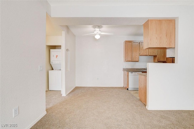 kitchen featuring stacked washer and clothes dryer, white dishwasher, light colored carpet, a ceiling fan, and baseboards