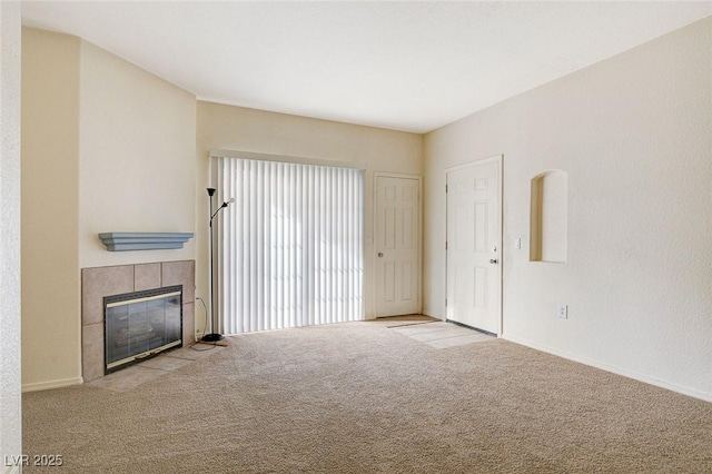 unfurnished living room featuring carpet, a tiled fireplace, and baseboards
