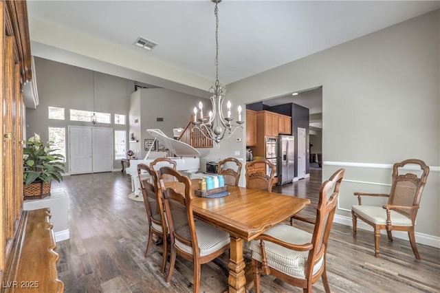 dining space featuring a chandelier, wood finished floors, baseboards, and a towering ceiling