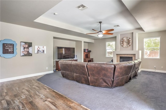 living area featuring a fireplace, baseboards, a ceiling fan, and dark wood-style floors