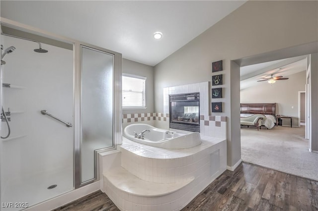 ensuite bathroom with lofted ceiling, a shower stall, a garden tub, a tiled fireplace, and wood finished floors