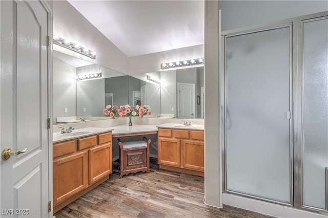 bathroom featuring wood finished floors, a stall shower, double vanity, and vaulted ceiling