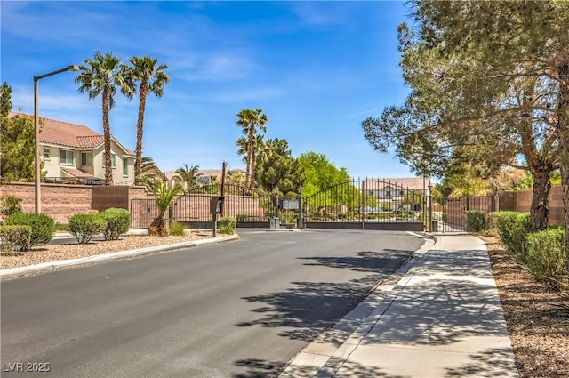 view of asphalt road featuring sidewalks, curbs, a gate, and a gated entry