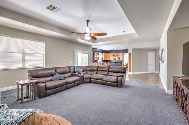 living room featuring dark colored carpet, baseboards, ceiling fan, and a tray ceiling