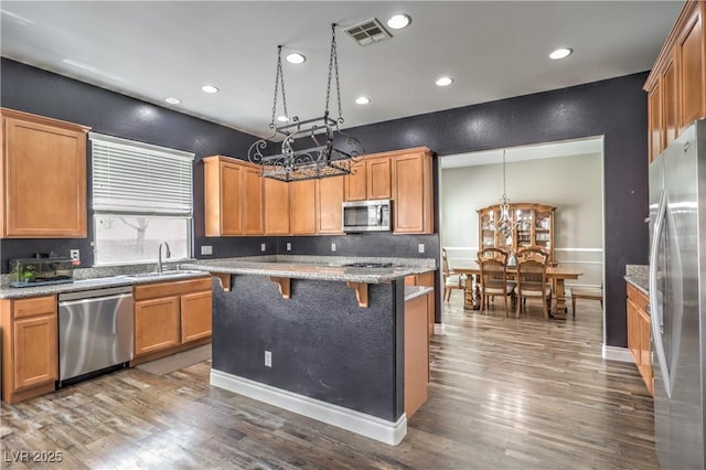 kitchen featuring appliances with stainless steel finishes, a chandelier, a sink, a breakfast bar, and wood finished floors
