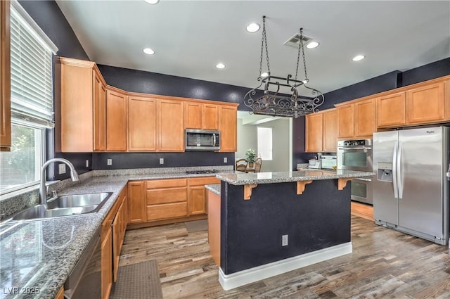 kitchen featuring appliances with stainless steel finishes, a sink, light wood finished floors, recessed lighting, and a breakfast bar