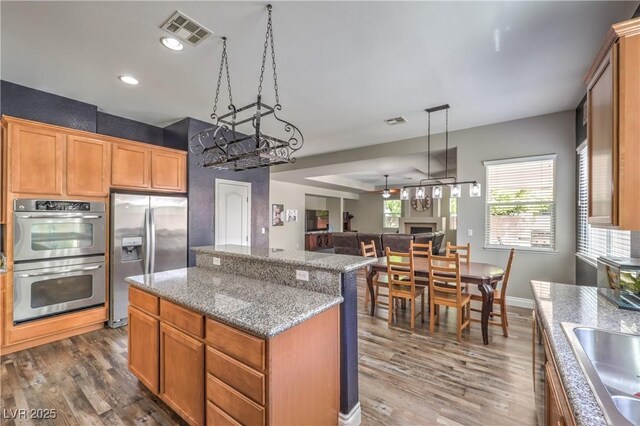 kitchen with appliances with stainless steel finishes, a center island, dark wood-style floors, a sink, and light stone counters