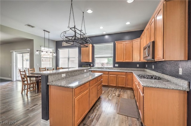 kitchen featuring stainless steel appliances, wood finished floors, stone countertops, a kitchen island, and hanging light fixtures