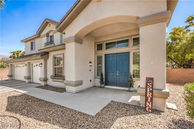 view of exterior entry with stucco siding, concrete driveway, a garage, and fence