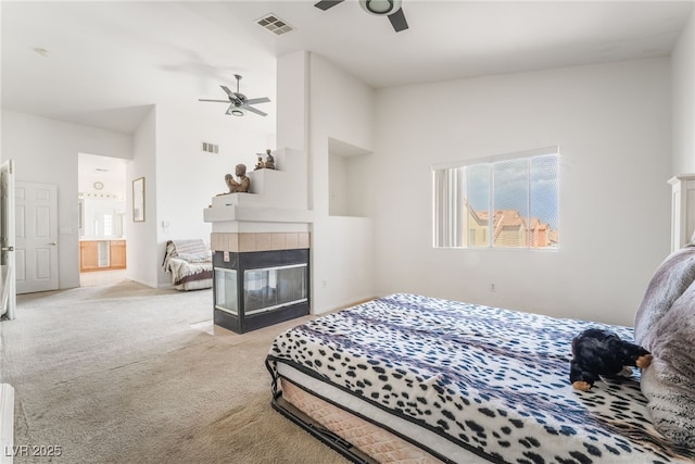 bedroom featuring a tile fireplace, multiple windows, carpet flooring, ensuite bath, and vaulted ceiling