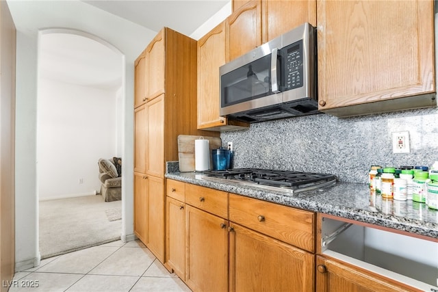 kitchen with appliances with stainless steel finishes, dark stone counters, light carpet, decorative backsplash, and light tile patterned flooring