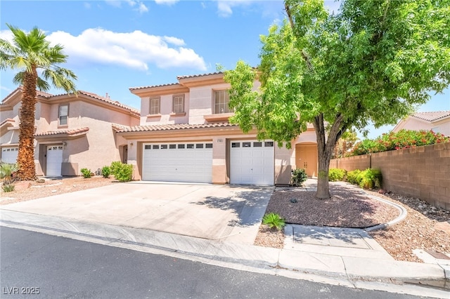 mediterranean / spanish-style house with stucco siding, driveway, a tiled roof, a garage, and fence