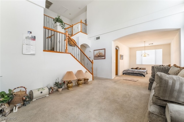 carpeted living area with arched walkways, stairs, and a high ceiling