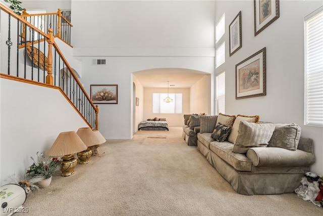 living area featuring arched walkways, carpet, a towering ceiling, stairs, and a chandelier