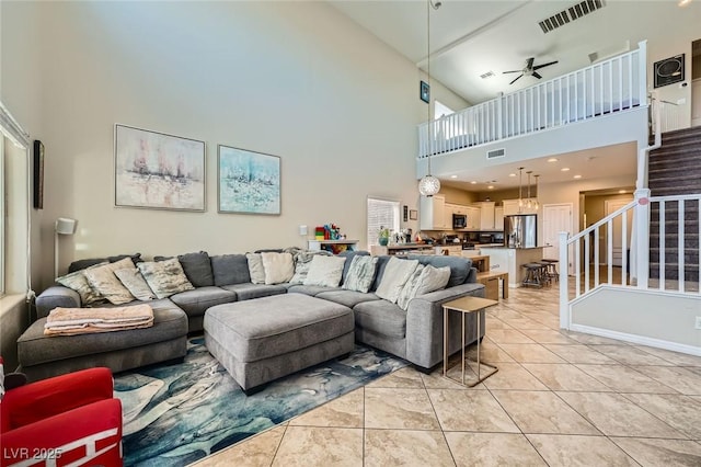 living room featuring a towering ceiling, ceiling fan, stairs, and light tile patterned flooring