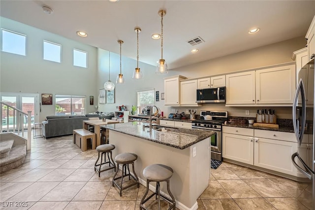 kitchen featuring appliances with stainless steel finishes, a sink, open floor plan, dark stone countertops, and light tile patterned floors