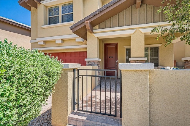doorway to property with a garage, a gate, fence, board and batten siding, and stone siding