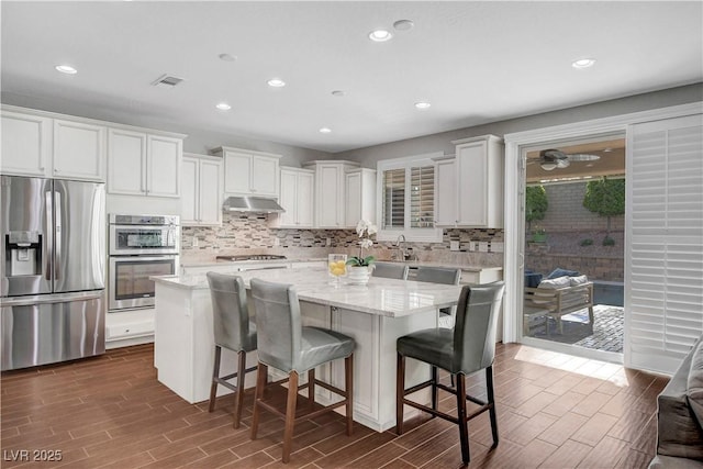 kitchen with stainless steel appliances, under cabinet range hood, wood tiled floors, tasteful backsplash, and recessed lighting