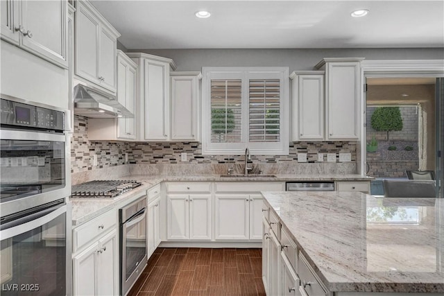 kitchen with a sink, under cabinet range hood, stainless steel appliances, recessed lighting, and decorative backsplash