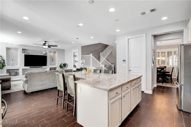 kitchen with freestanding refrigerator, a kitchen bar, dark wood finished floors, recessed lighting, and white cabinetry