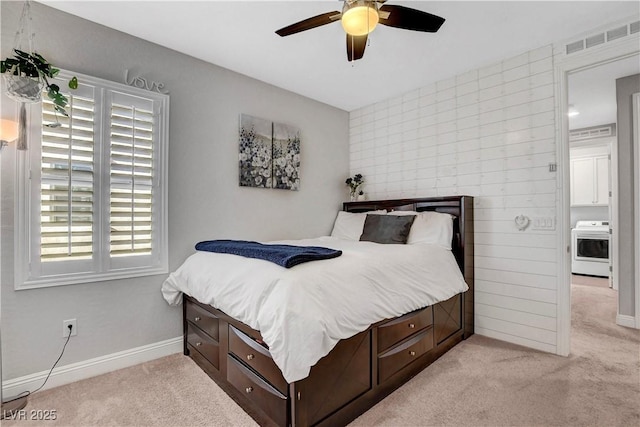 bedroom featuring light colored carpet, washer / dryer, baseboards, and ceiling fan