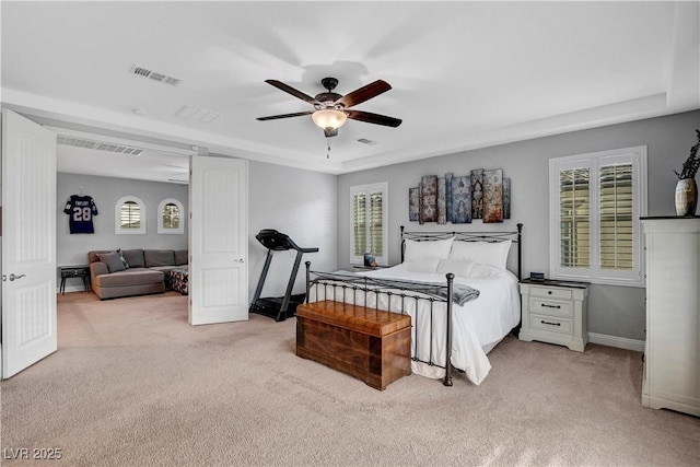 carpeted bedroom featuring multiple windows, a tray ceiling, baseboards, and a ceiling fan