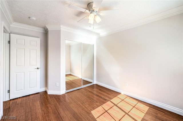 unfurnished bedroom with wood finished floors, a closet, baseboards, crown molding, and ceiling fan