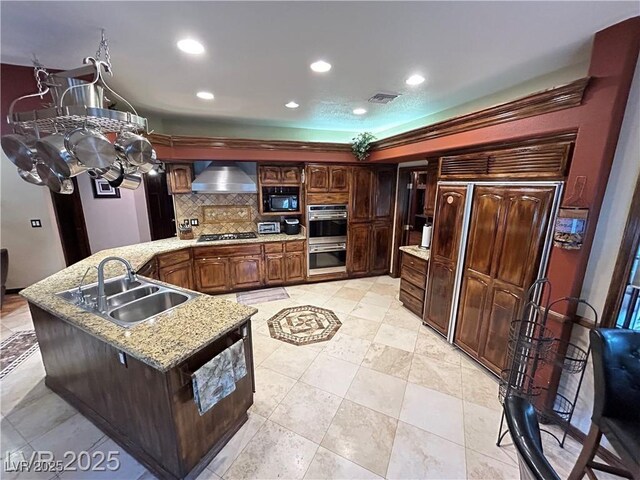 kitchen featuring a sink, appliances with stainless steel finishes, wall chimney range hood, decorative backsplash, and a peninsula