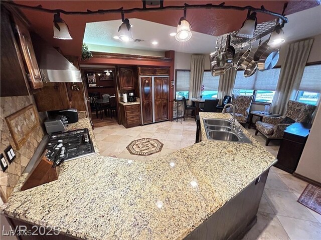 kitchen with a sink, exhaust hood, stainless steel gas stovetop, light tile patterned flooring, and dark brown cabinets