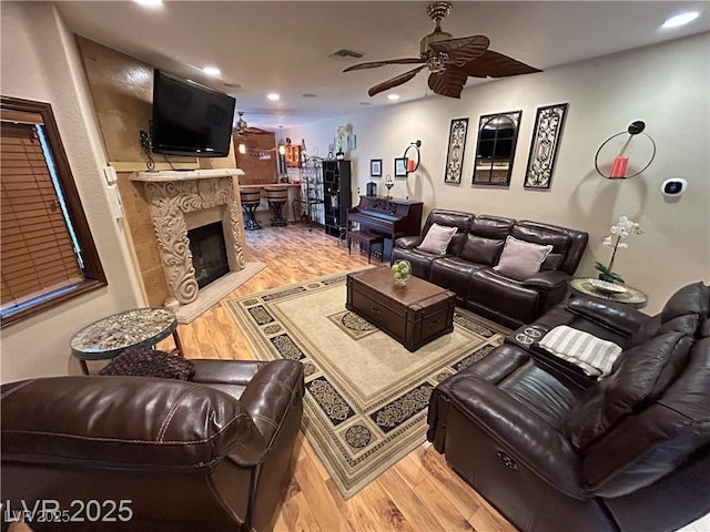 living room with light wood-style flooring, ceiling fan, recessed lighting, and a premium fireplace