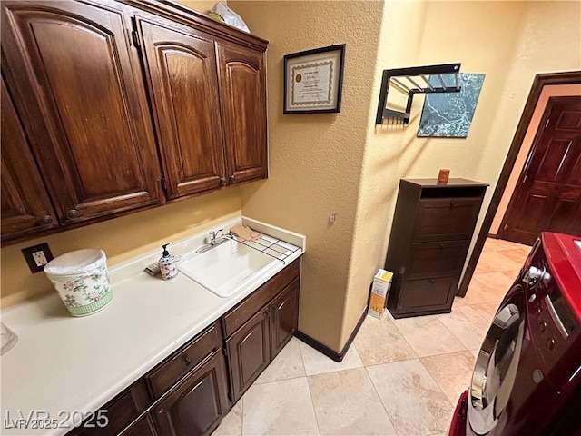 washroom with cabinet space, baseboards, a textured wall, and light tile patterned floors