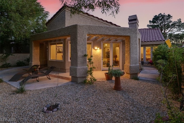 5142 Southern Hills Ln, Las Vegas, NV 89113 - back of property at dusk featuring stucco siding, a chimney, a patio area, and a tiled roof