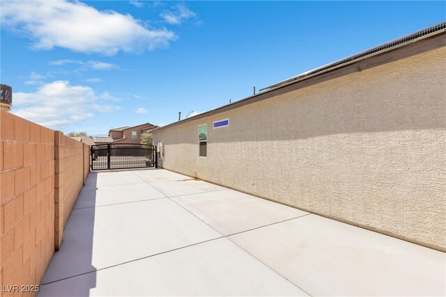 view of property exterior with fence, a gate, stucco siding, and a patio